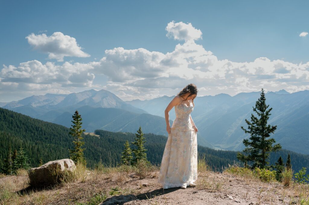 photograph by laura stone photo of bride standing on top of mountain with landscape view at aspen mountain wedding venue