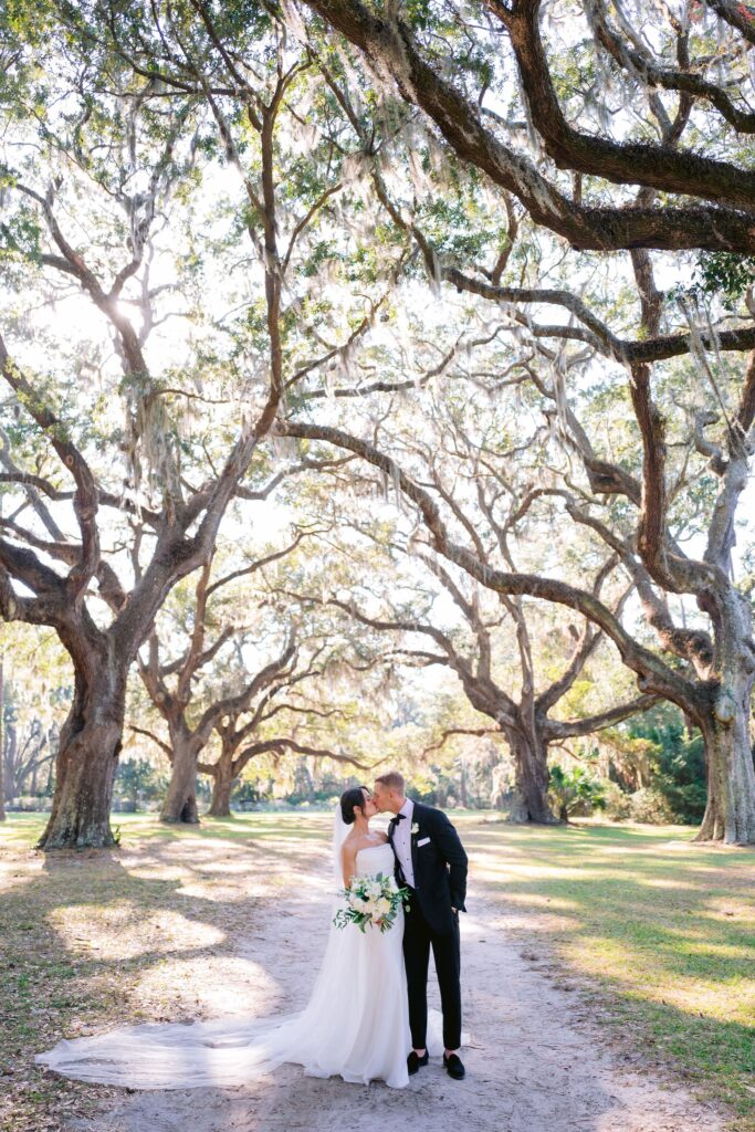 portrait by laura stone photo of bride and groom staring lovingly kissing under the oak trees at the Six Oaks Cemetery before their sea pines resort wedding ceremony