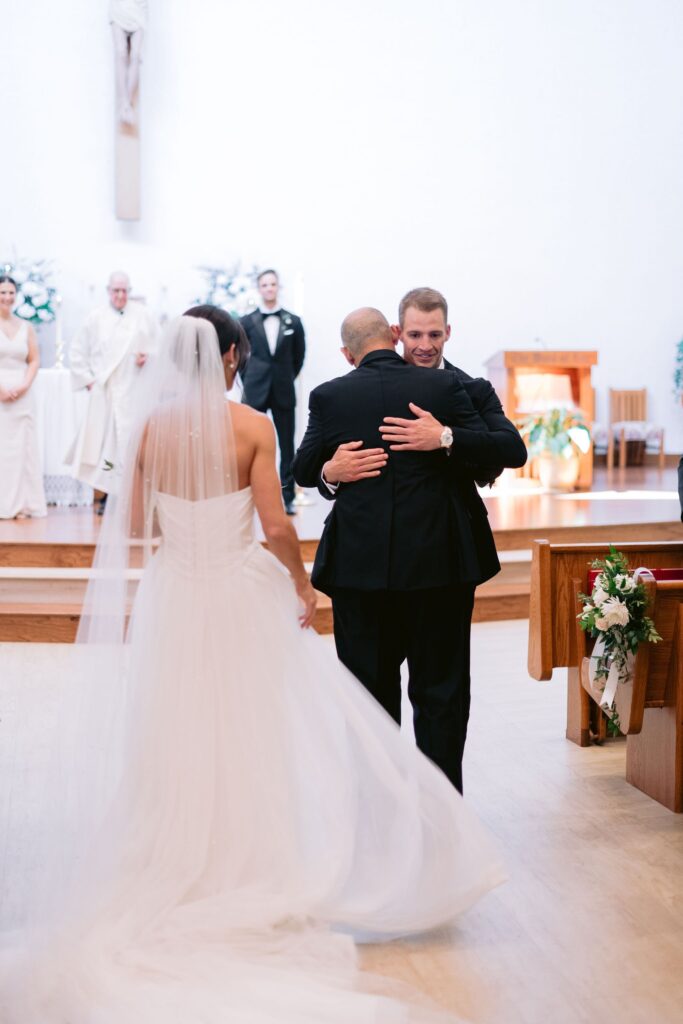 father hugging groom in St. Francis by the Sea Catholic Church