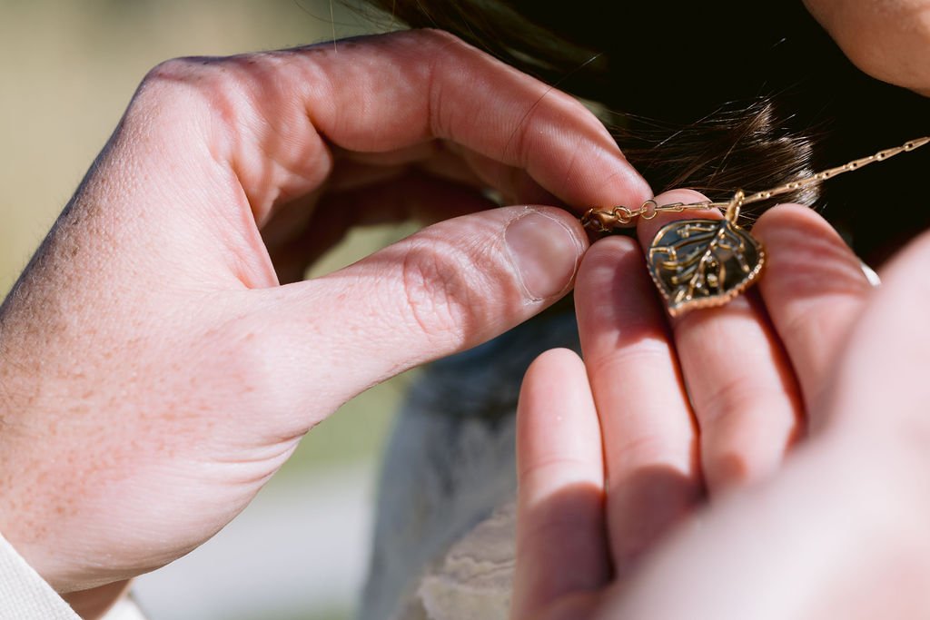 close up of a groom holding his bride's heart-shaped necklace during their aspen meadows wedding portrait session
