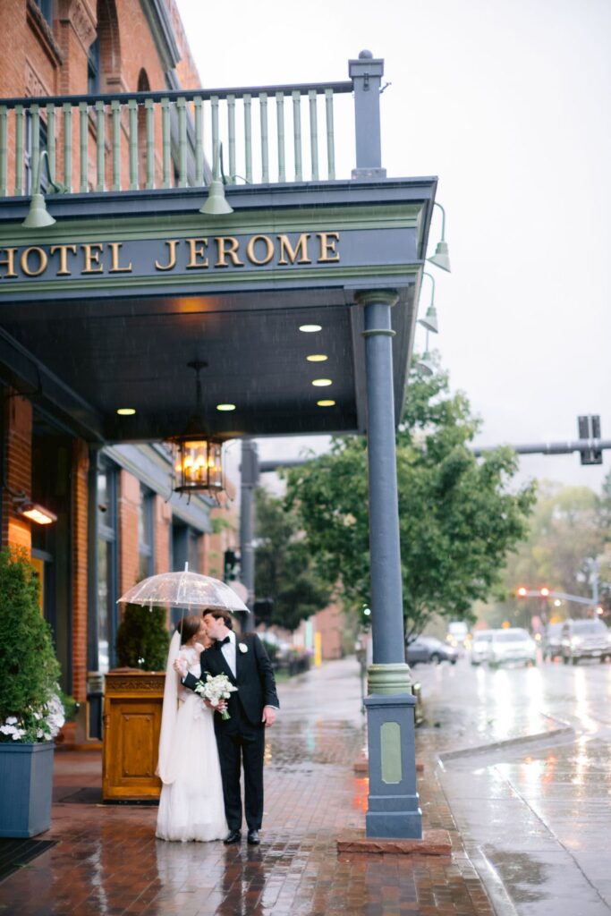 bride and groom sharing a kiss under a transparent umbrella in front of hotel jerom during their aspen wedding