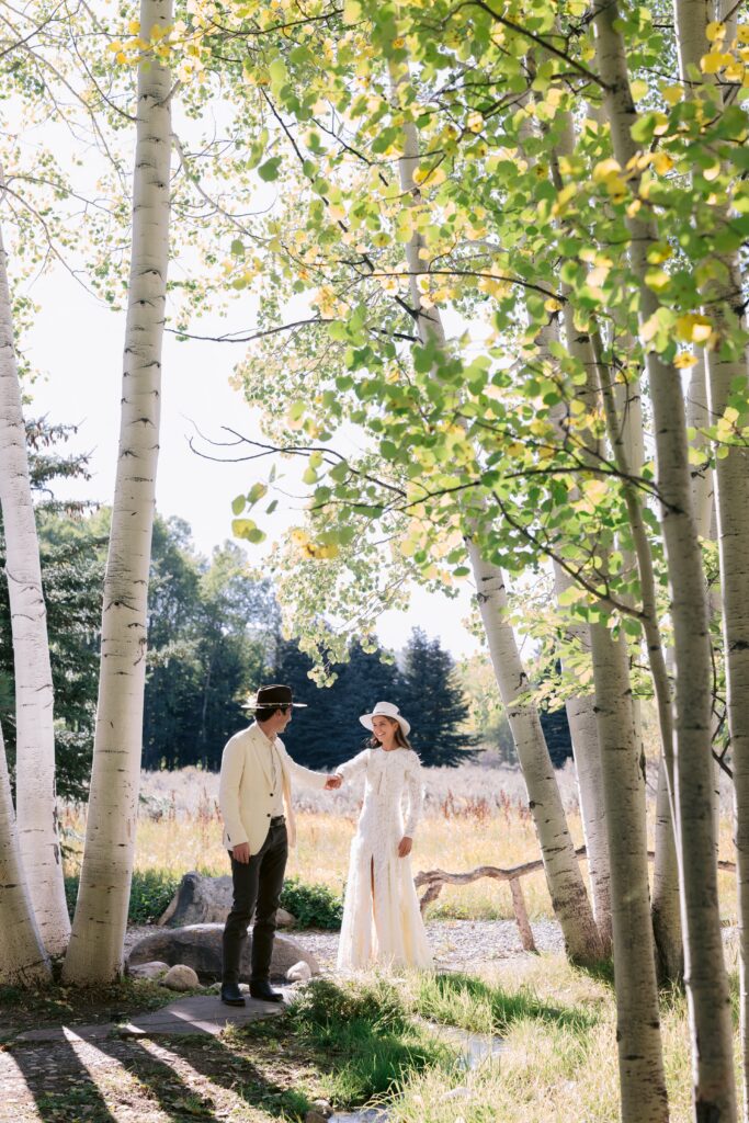 bride and groom holding hands beneath aspen trees during an intimate gathering in aspen colorado