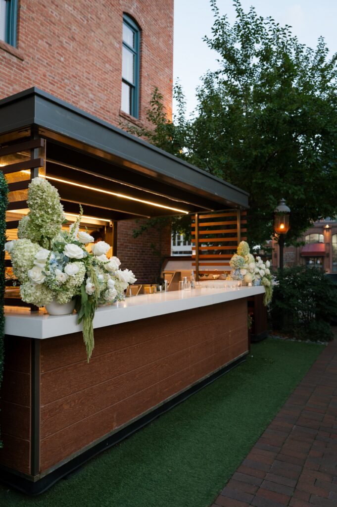 outdoor cocktail bar with lush white florals at an Aspen luxury wedding planner designed event in a perfect setting in Aspen Colorado