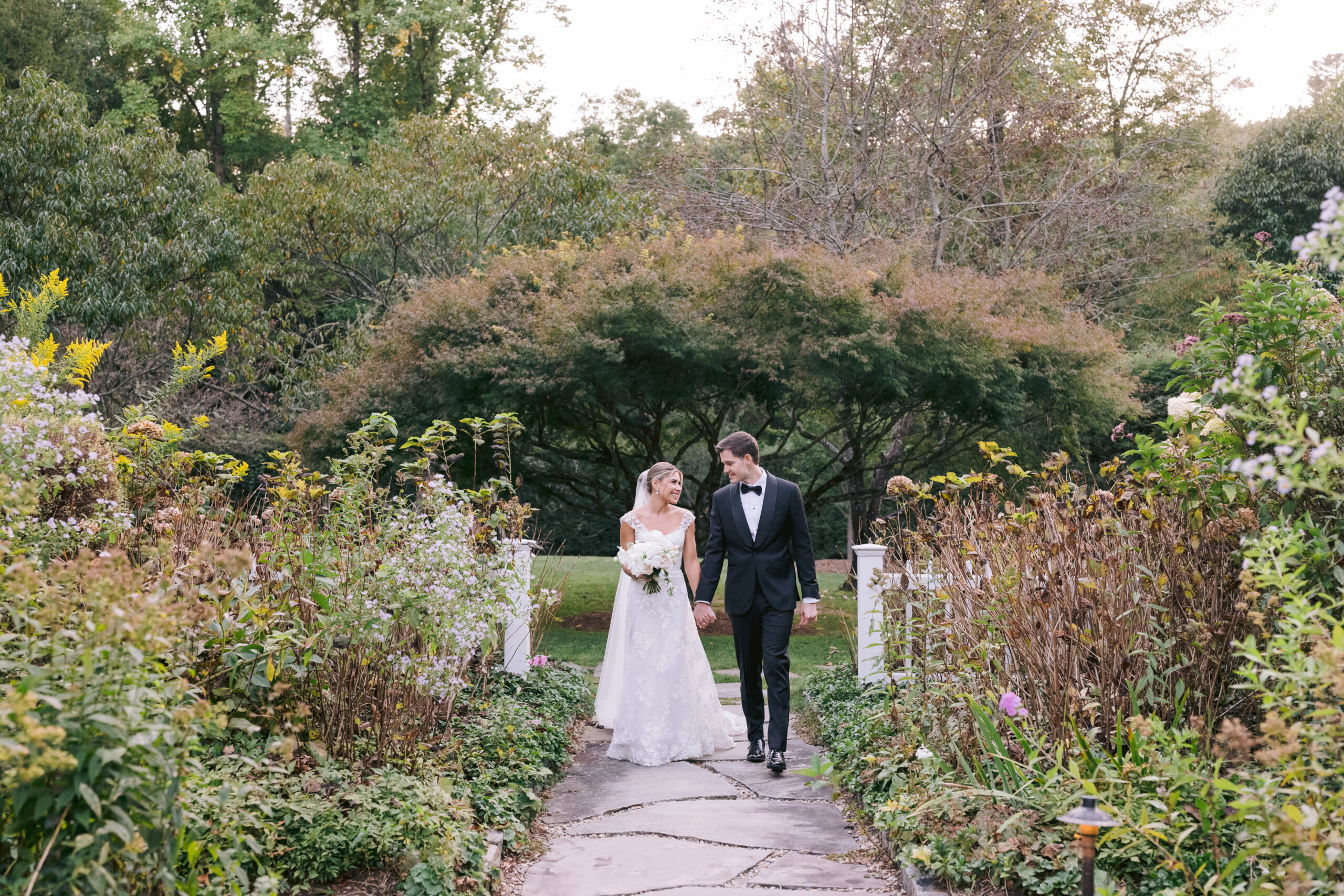 bride and groom holding hand while walking through a garden path during their wedding portraits at half-mile farm north carolina