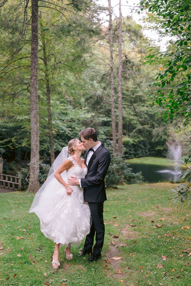bride and groom sharing a kiss on the lawn surrounded by greenery, trees and a lake at old edwards half-mile farm