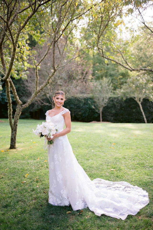 beautiful portrait of a bride standing on the lawn with her bouquet in hand, smiling at the camera during her half-mile farm north carolina wedding