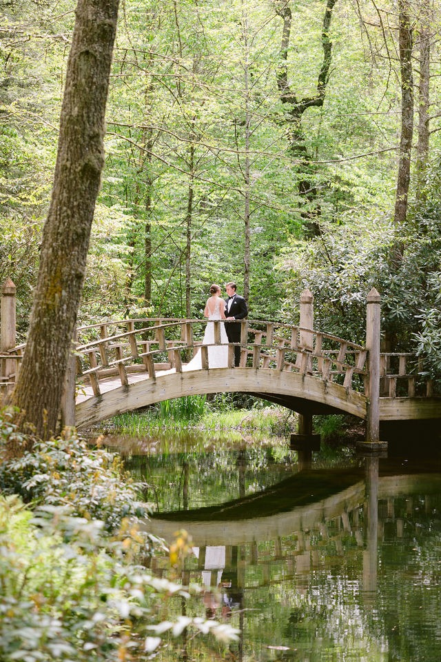 bride and groom standing on a wooden bridge at one of the most sought after wedding venues in highlands nc