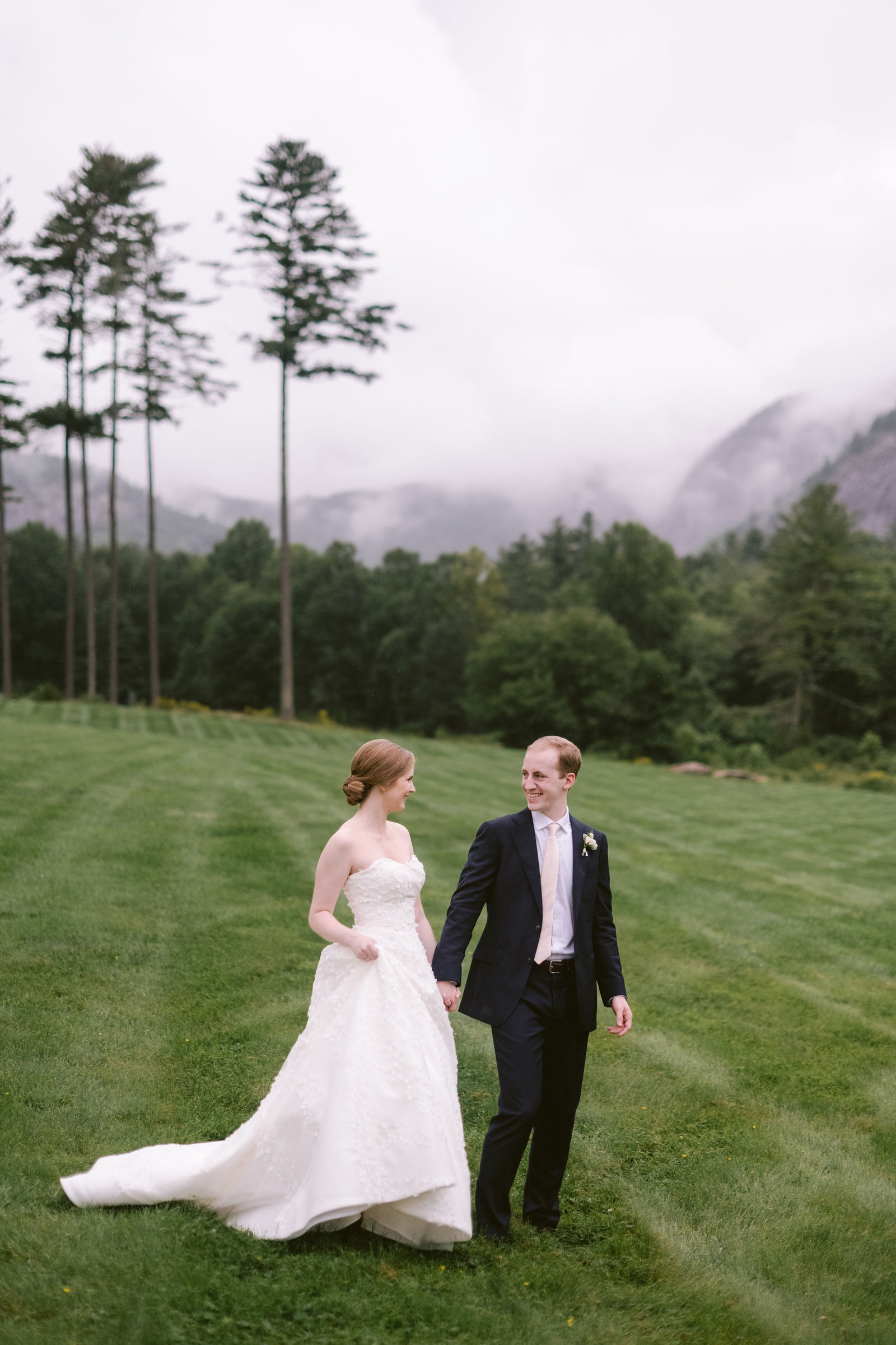 bride and groom walking hand in hand on the expansive lawn at a highlands nc wedding venue during their portrait session