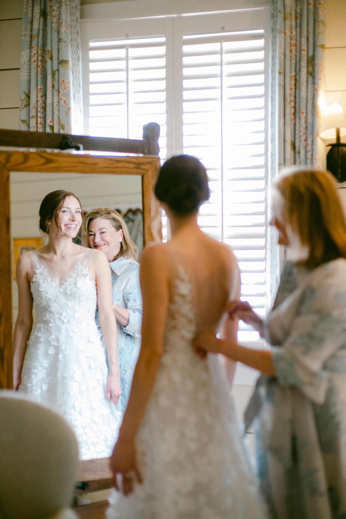Bride smiling in the mirror while getting ready with her mother before the wedding.