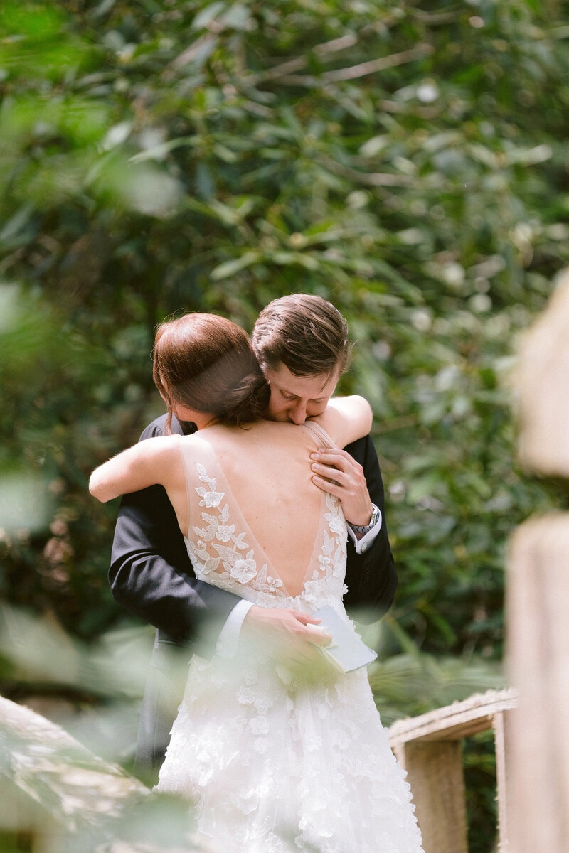 Bride and groom embracing on a wooded path surrounded by greenery