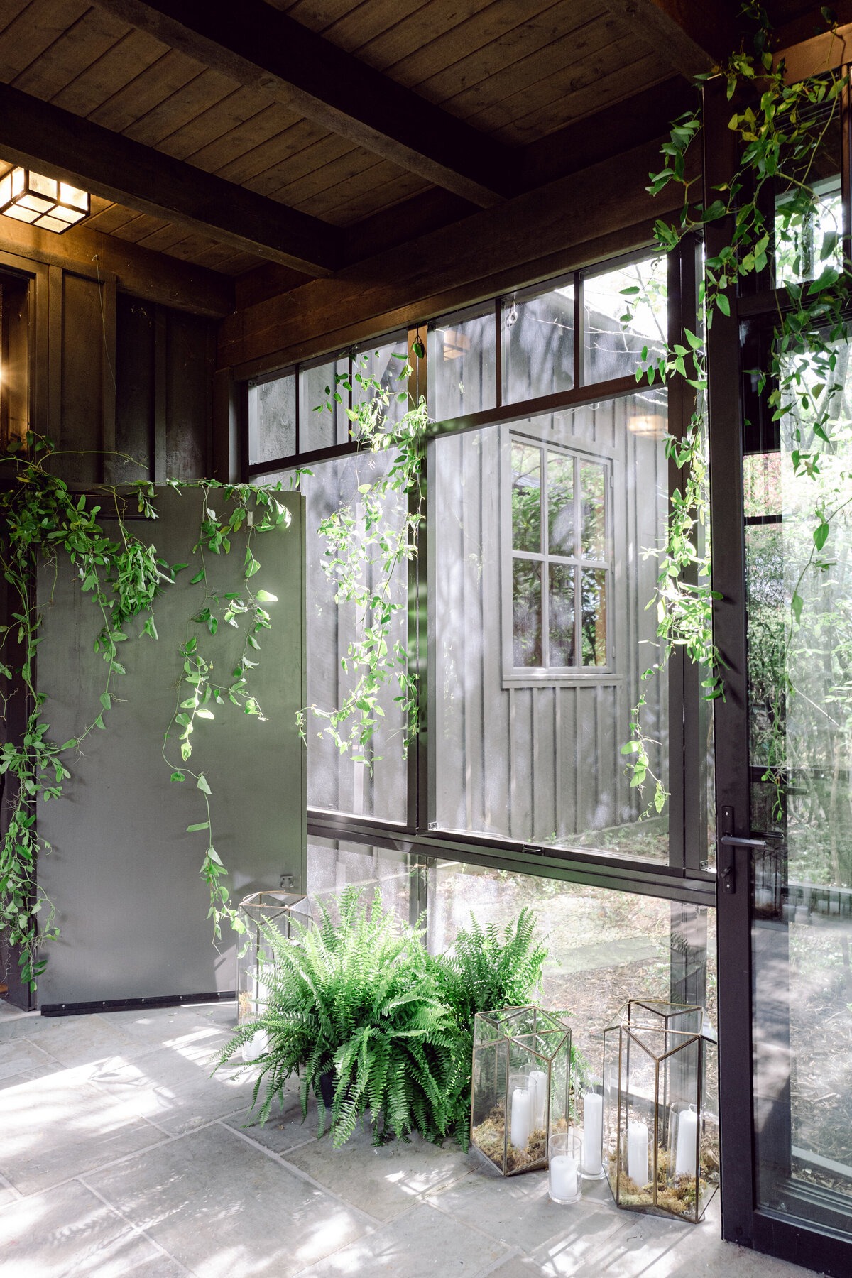 Sunlit glass wedding space decorated with cascading greenery, ferns, and candles.