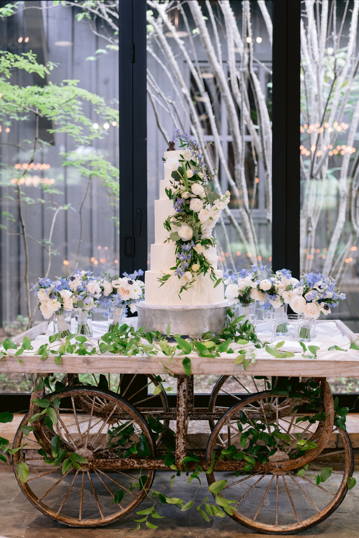 Tiered white wedding cake decorated with cascading white and blue flowers and greenery.